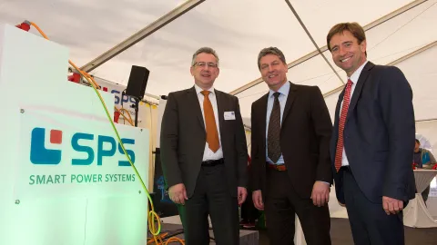 three people in suits standing in a tent next to a white cube
