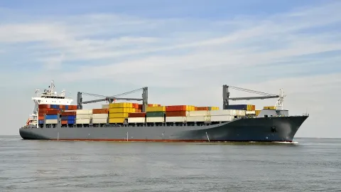 grey cargo ship seen from a side perspective, not many containers on it