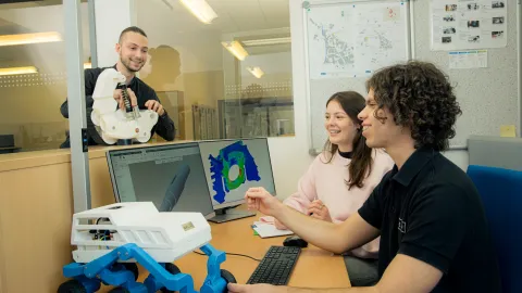 Several people discuss technical models and design data at a workstation.