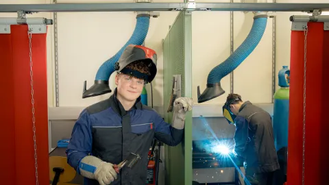 A person presents welding work while welding is taking place in the background.