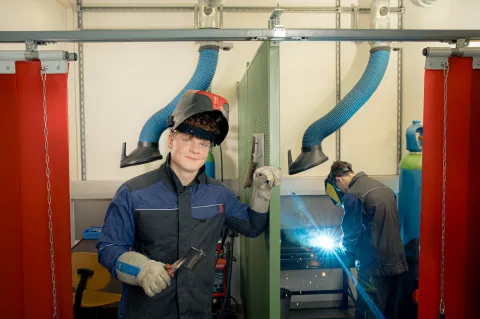 A person presents welding work while welding is taking place in the background.