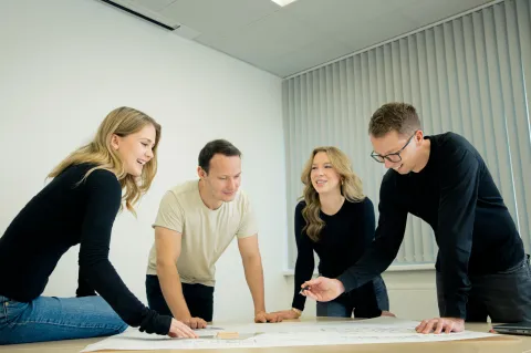 Several people collaborate on technical plans and drawings.